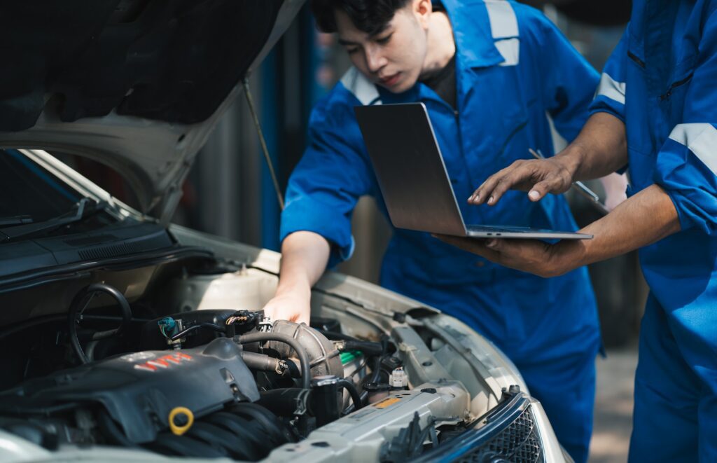 Two auto mechanic working with car diagnostic tool in a repair shop.